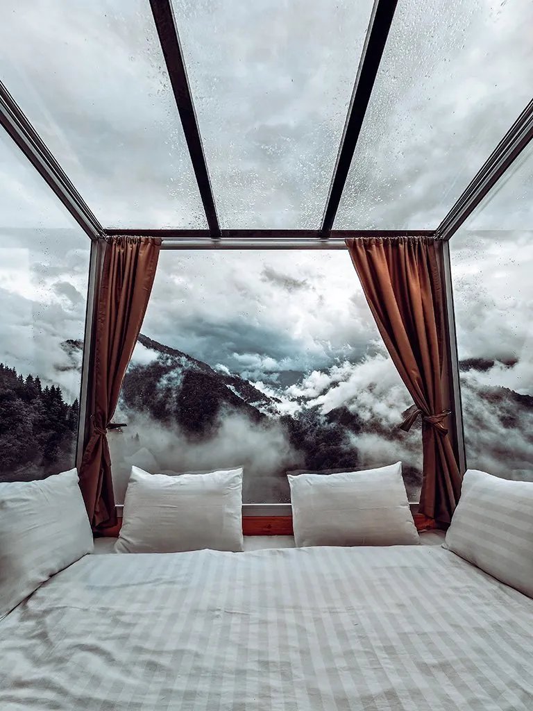 A glass-roofed bedroom at Eco House Merisi looking out at clouds over the mountains