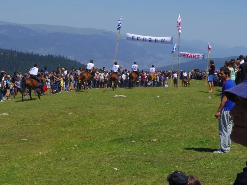 მხედრები ცხენების რბოლის სტარტზე შუამთობაზე, მდელოზე ხალხით