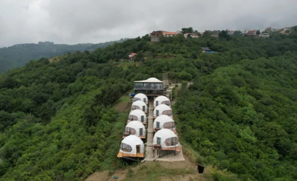 Signagi Glamping-ის თეთრი გუმბათების რიგი ტყიან ფერდობზე, ზემოდან