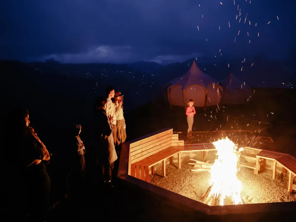 სტუმრები კოცონთან Glamping Tago-ში ღამით, უკან განათებული კარავი