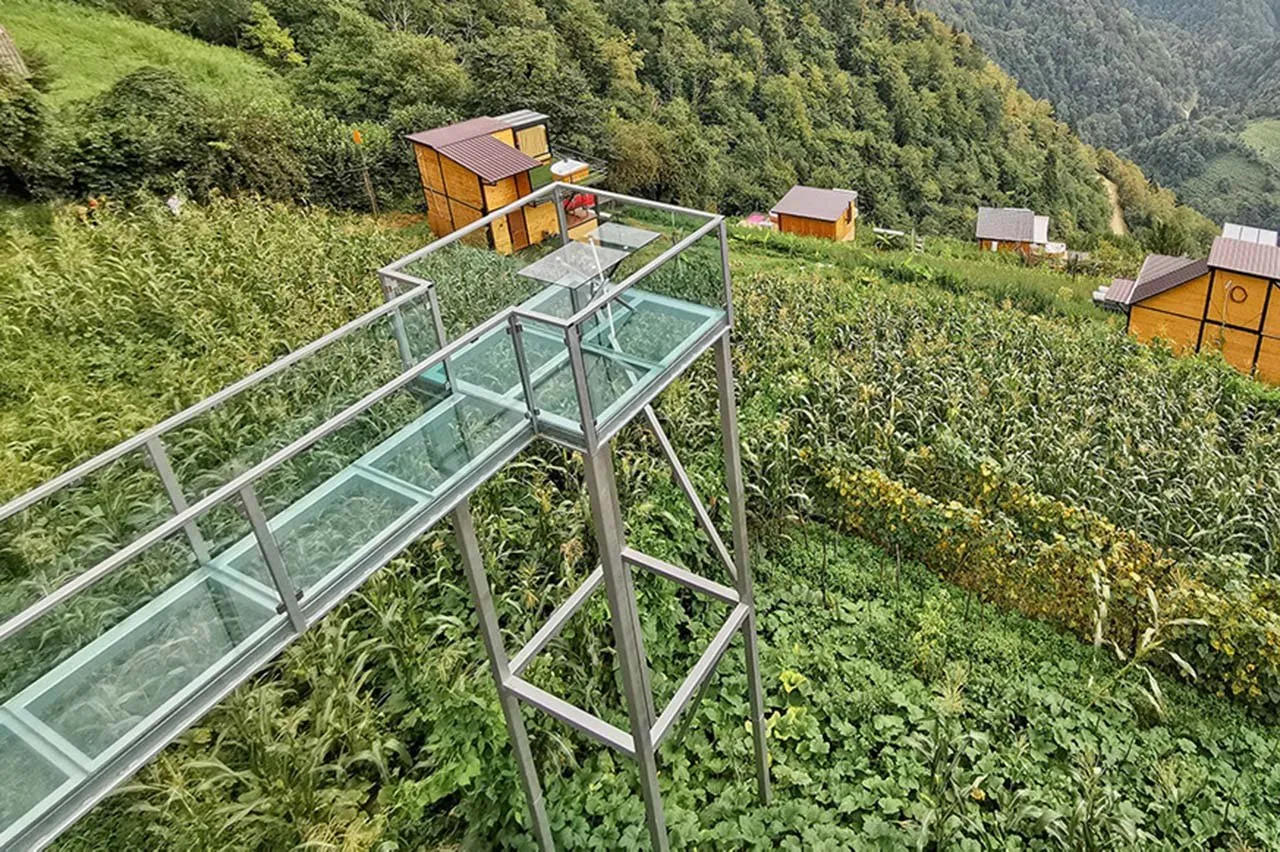 A glass walkway above vegetable gardens with wooden cottages of Eco House Merisi