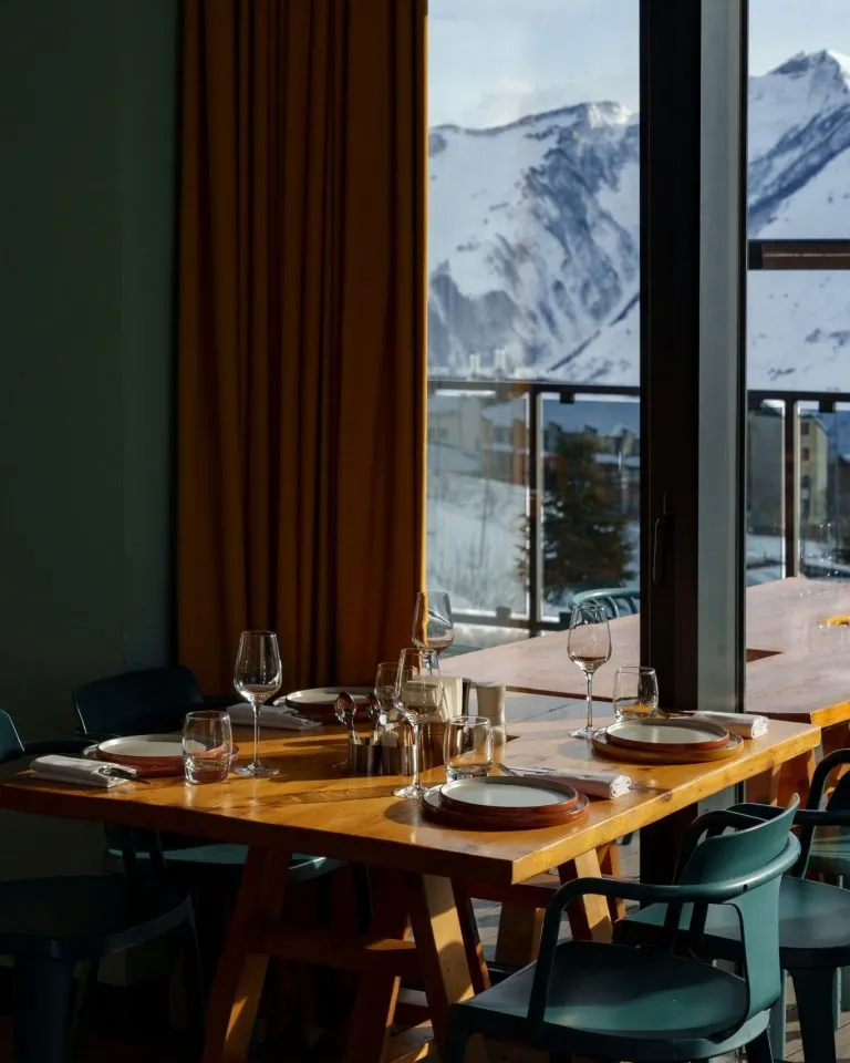 A set dinner table by tall windows with snowy mountains outside at Gudauri Lodge
