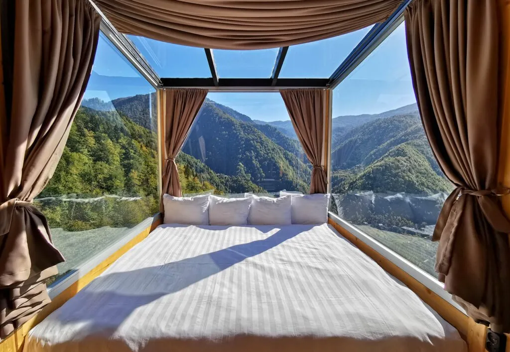 A bed in a glass cottage at Eco House Merisi looking out over the forested valley