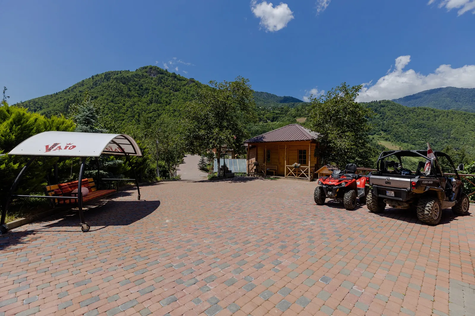 The courtyard of Vaio Resort with a wooden cottage and green hills behind