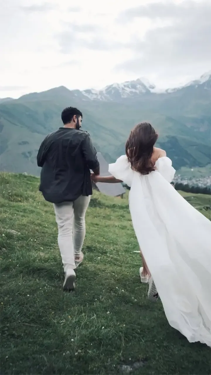 A couple walking hand in hand across a green mountain meadow