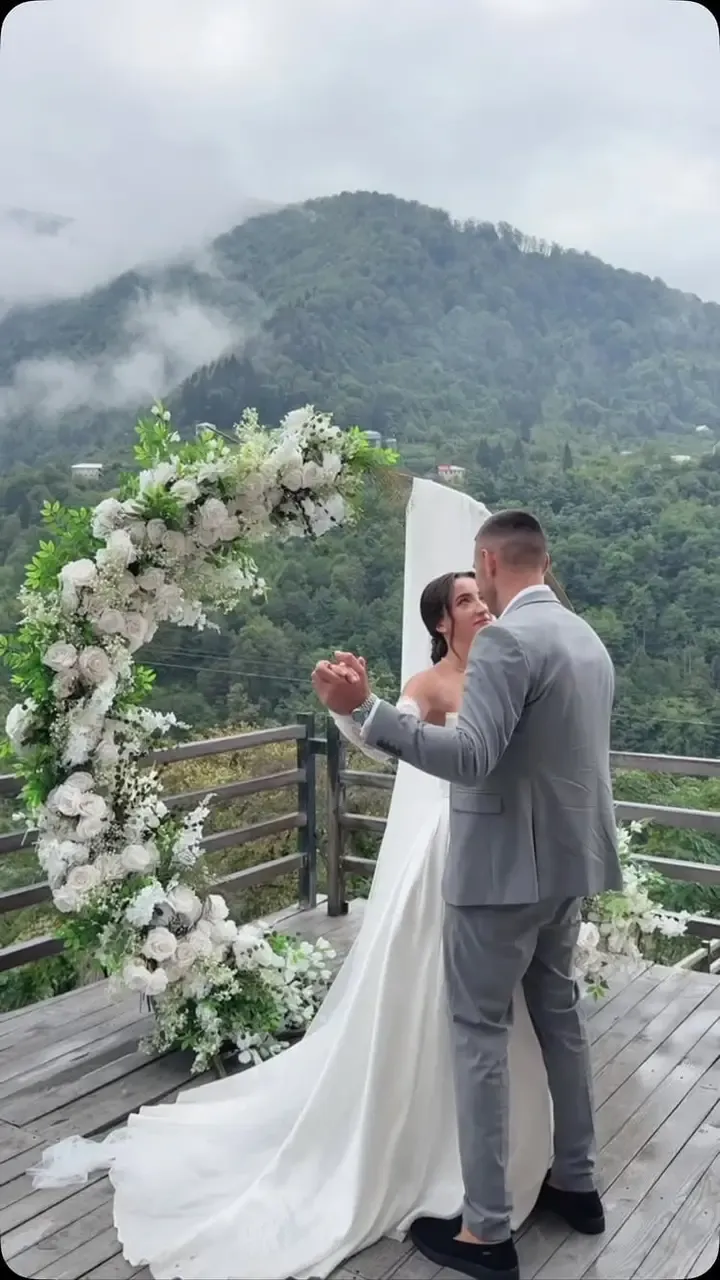 წყვილი ყვავილების თაღის ქვეშ ტერასაზე, უკან მწვანე ბორცვები