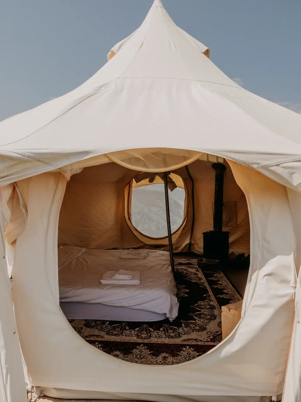 Inside a canvas guest tent: bed, rug and stove, with mountains outside