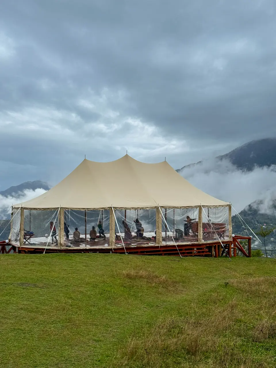 The large beige sailcloth tent on a green hill above misty mountains