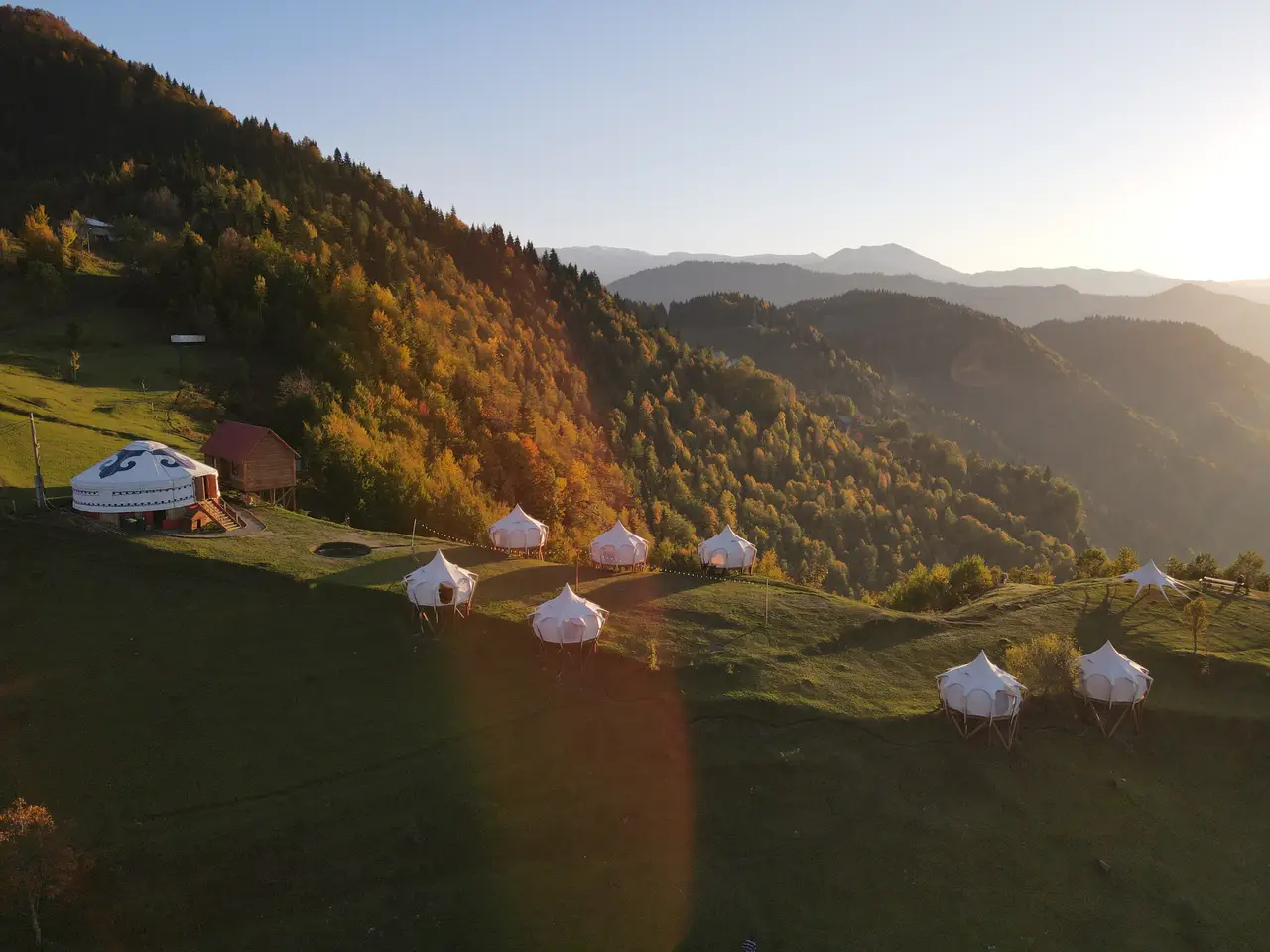 Вид с воздуха на шатры и юрту Glamping Tago на зелёном горном склоне на закате