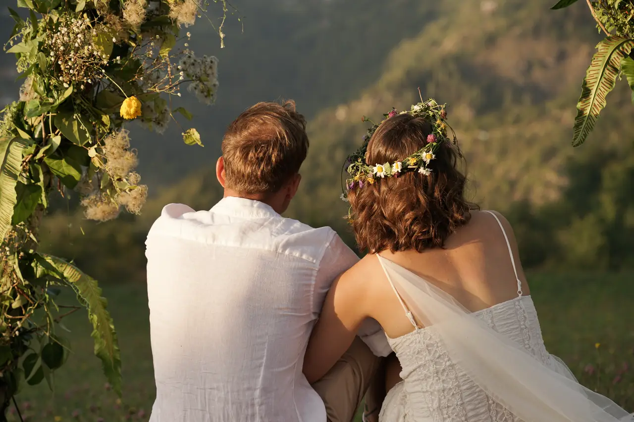 A couple seen from behind under a floral arch, looking out over the Adjara mountains