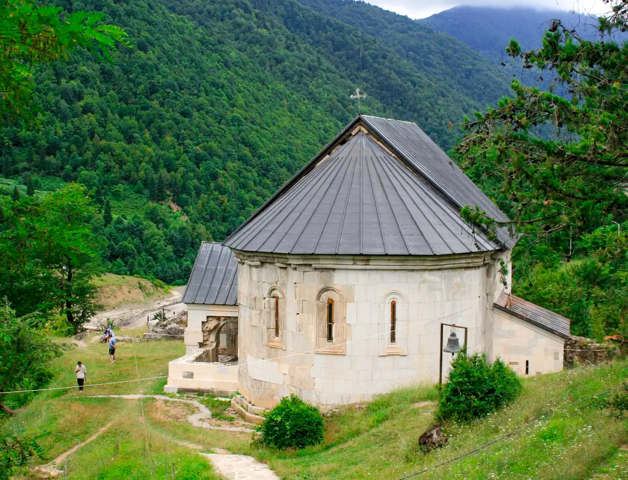 Церковь монастыря Схалта с тёмной крышей среди зелёных гор