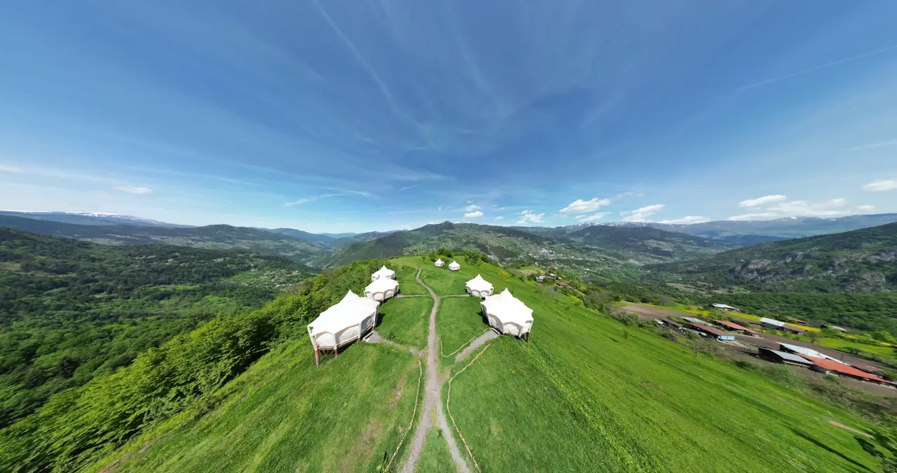 Aerial view of the white tents of Glamping Tago on a green ridge above Village Tago