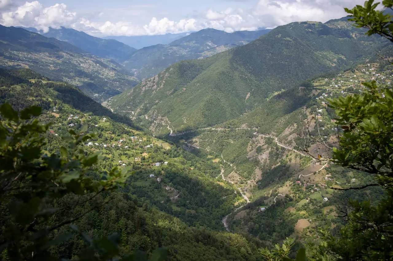 Green forested mountains and a valley with villages and a winding road in Adjara