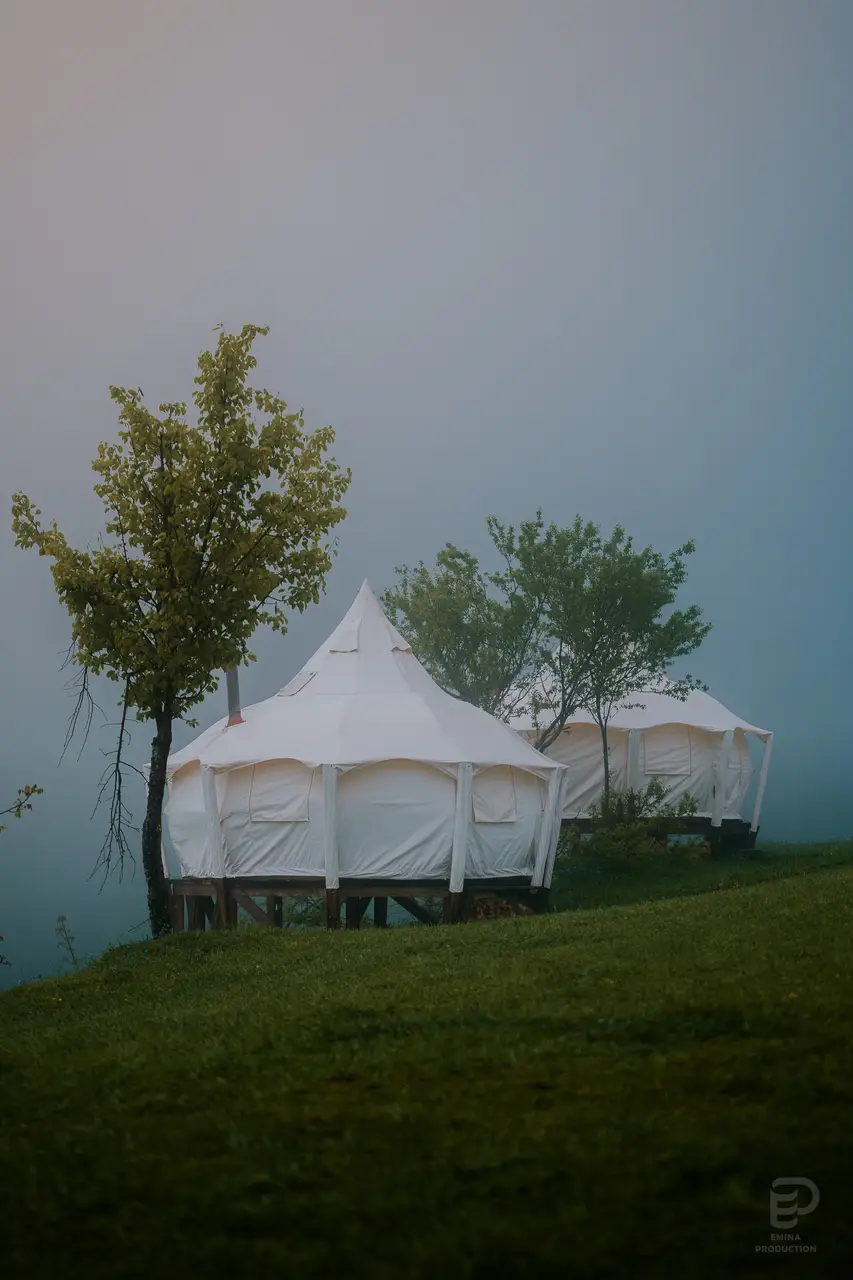 Два белых парусиновых шатра на деревянных настилах в Glamping Tago, над склоном поднимается туман