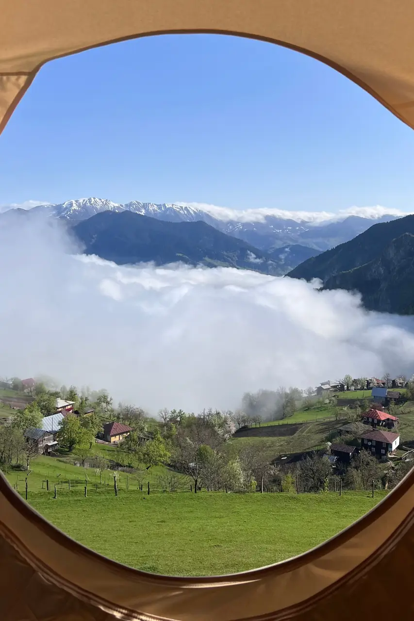 Вид из шатра в Glamping Tago на долину, заполненную облаками, и деревню внизу