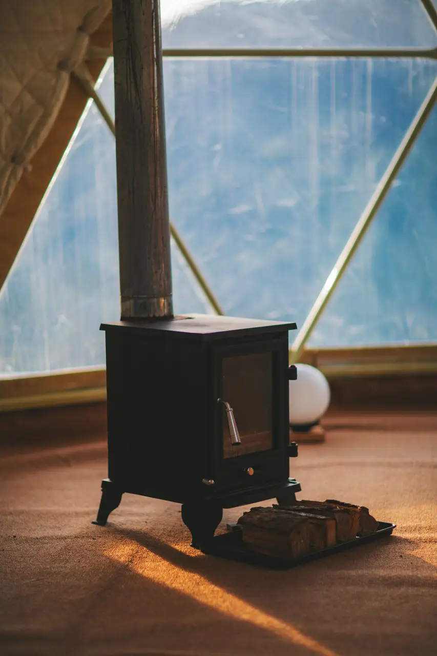 Wood stove and firewood inside the geodesic yoga dome with sunlight through the windows