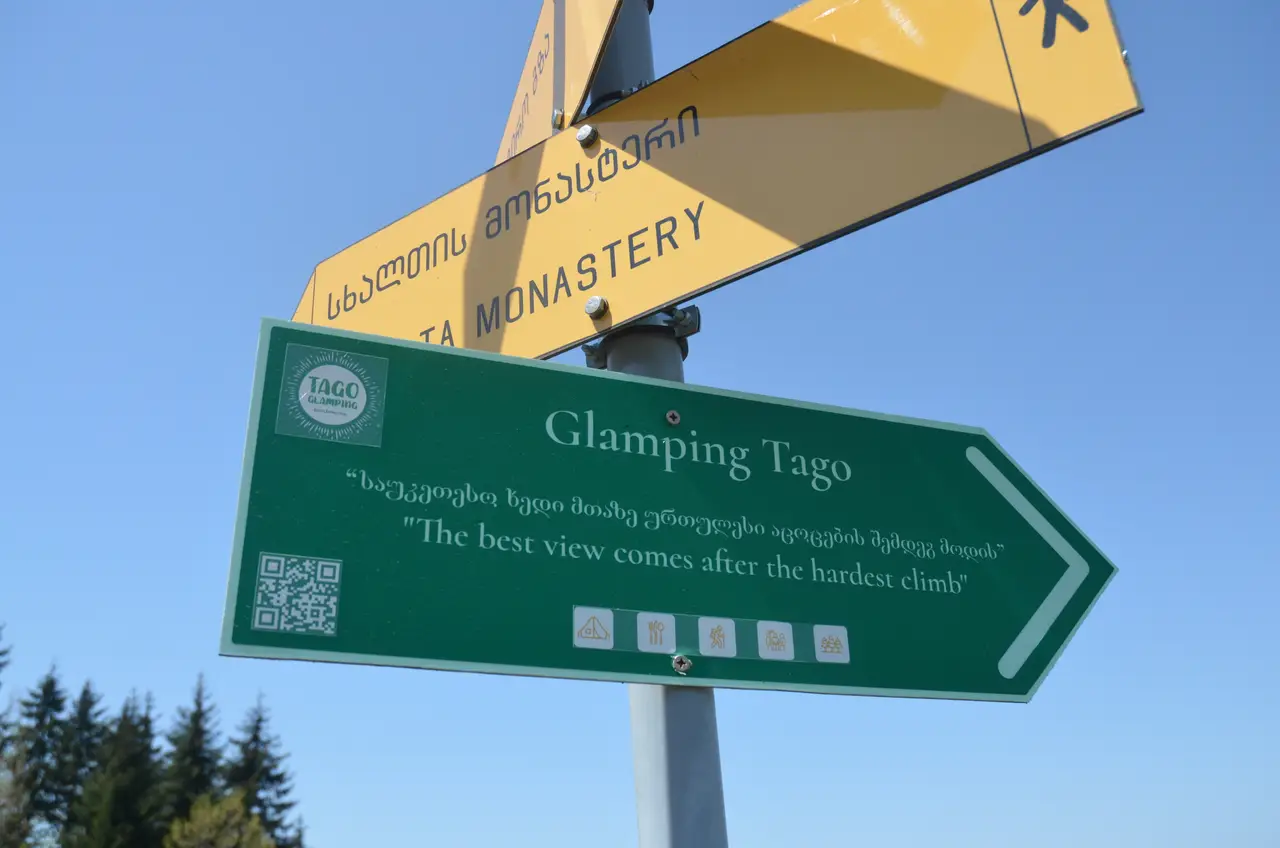 Green and yellow trail signpost pointing to Glamping Tago and Skhalta Monastery