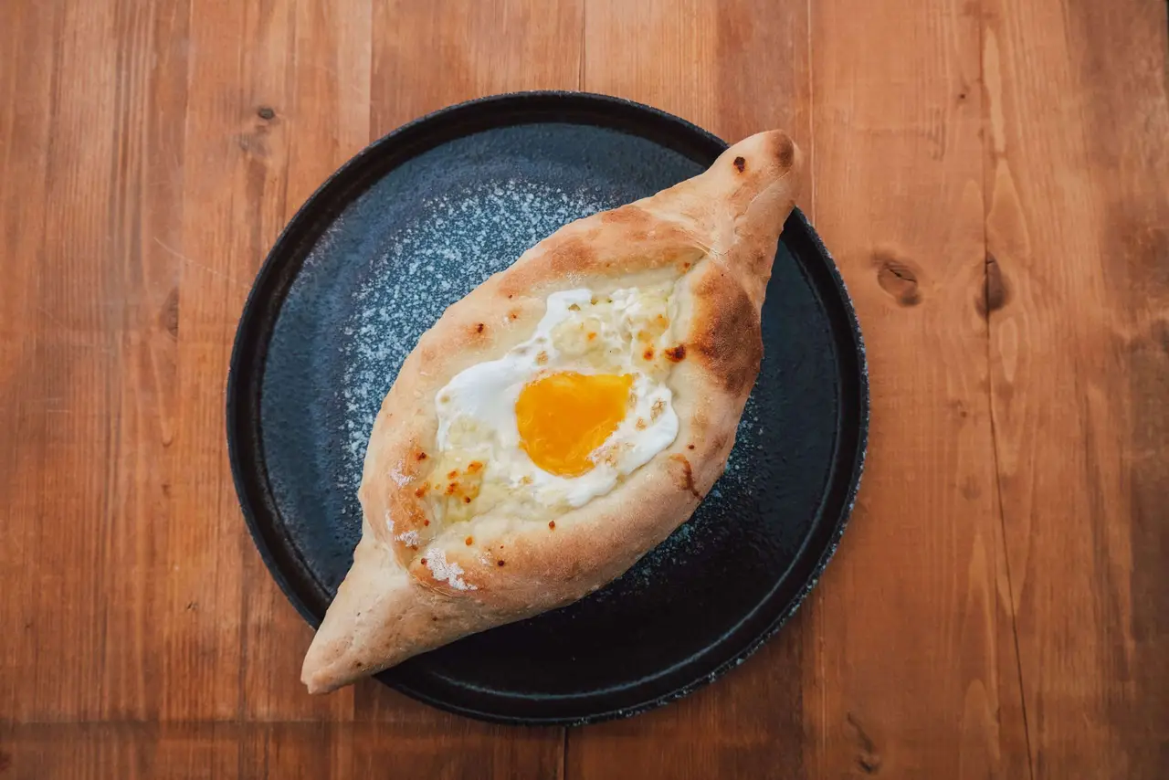 Boat-shaped Adjarian khachapuri with melted cheese and an egg yolk on a dark plate