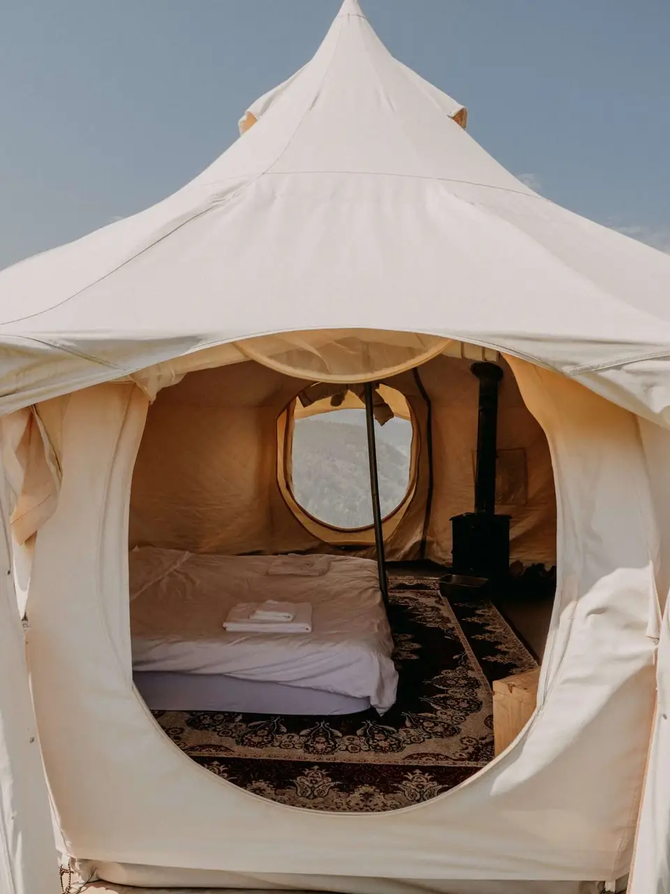 Inside a Lotus Belle tent: a bed, a wood stove and a round window onto the mountains