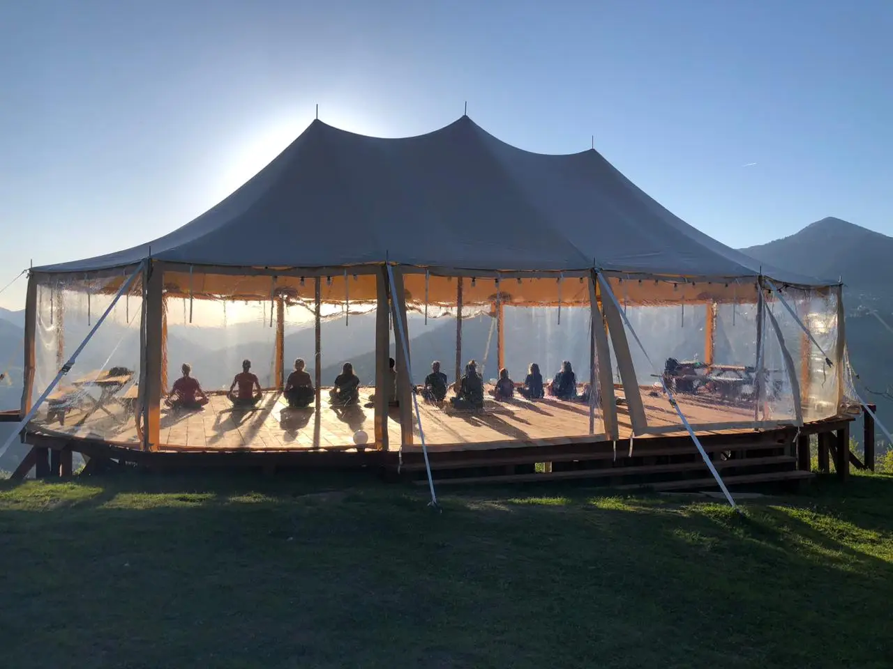 People meditating inside the sailcloth tent at sunset with mountains behind