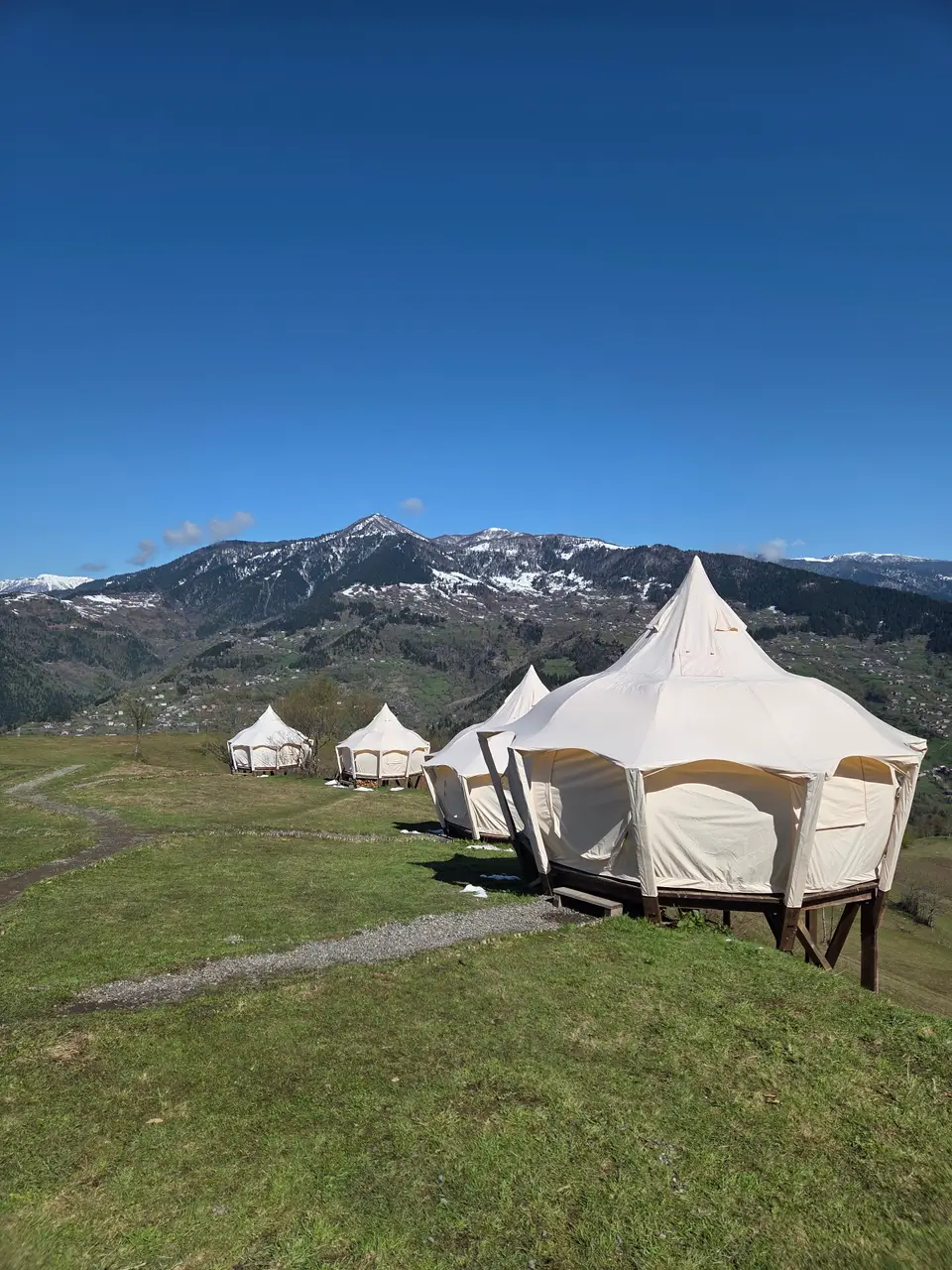 Canvas tents on a green hill with snow on the mountains behind in April