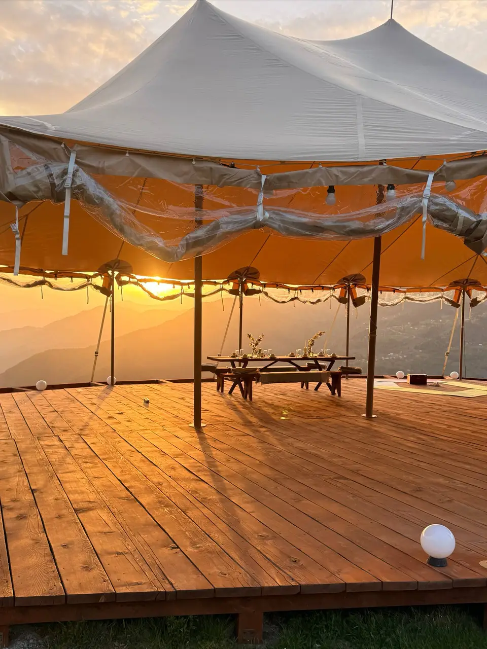 The sailcloth event tent at Glamping Tago with a dining table set on the wooden deck at sunset
