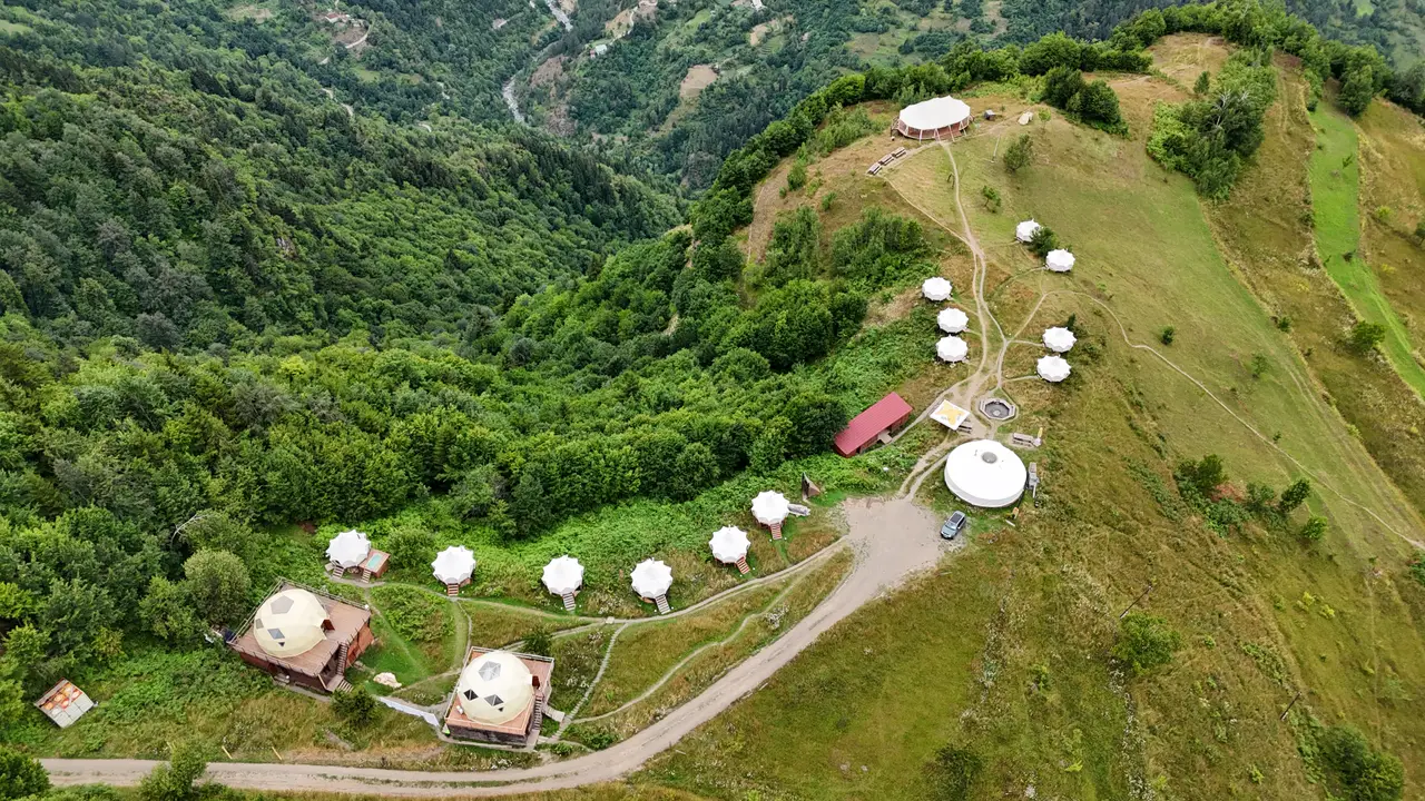 Вид сверху на Glamping Tago: белые палатки, купола и шатёр для событий на зелёном горном хребте