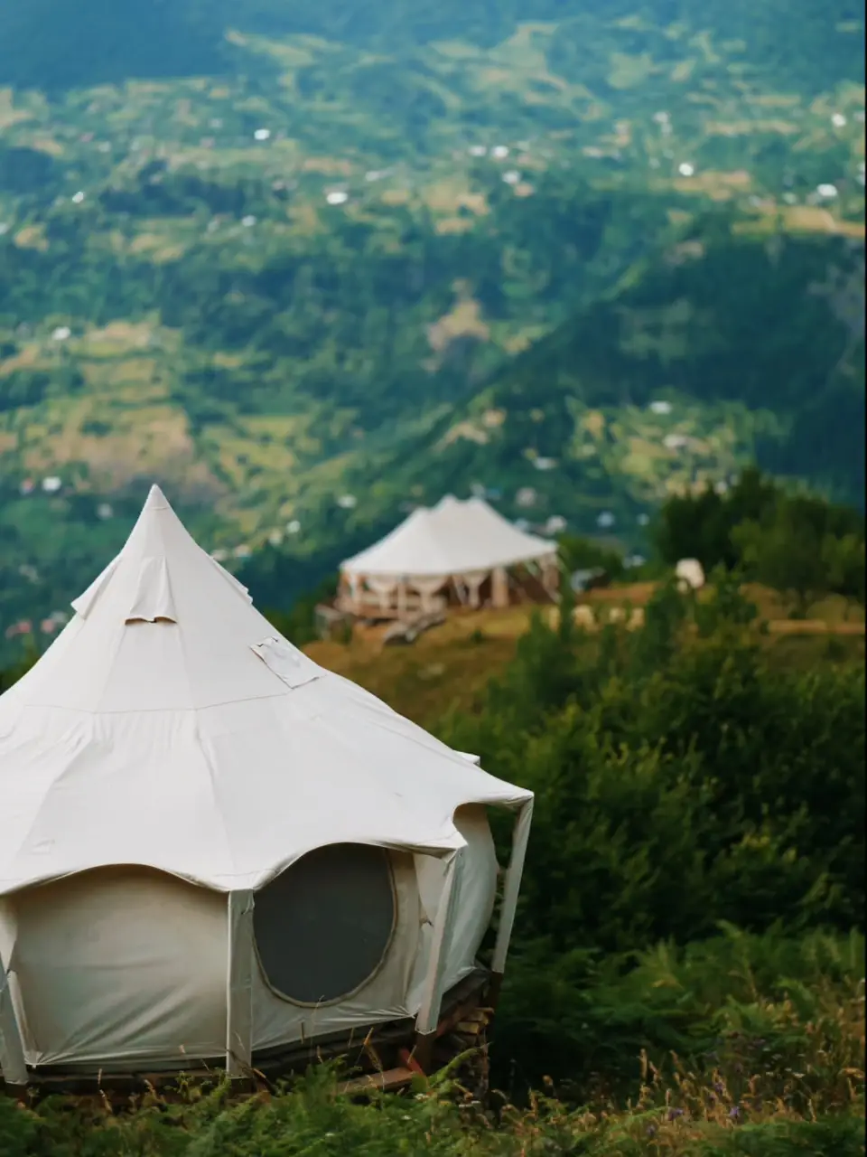 A white canvas guest tent on a hillside with green mountains behind