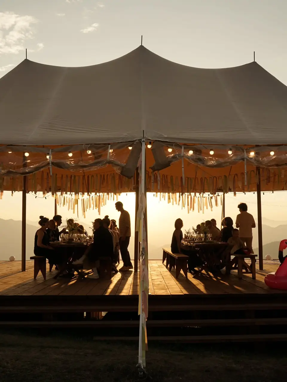 Guests dining under the big sailcloth tent at sunset with the mountains behind