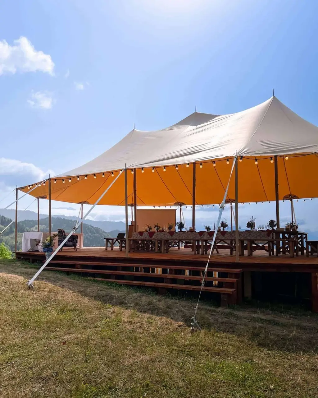 White and orange event tent with string lights and decorated tables on a wooden deck