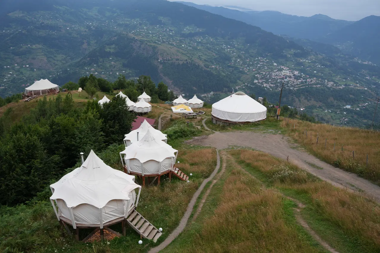 Вид сверху на белые шатры Glamping Tago на горном хребте над долиной с деревнями